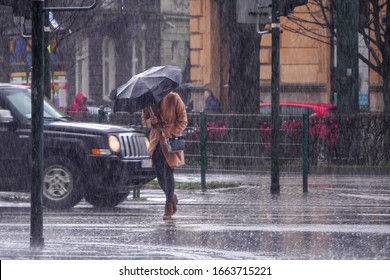 A woman in a brown coat under an umbrella crosses a busy street in heavy rain. Heavy precipitation in the city. Flooding of city streets. - Powered by Shutterstock