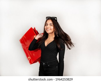 Woman with brown hair, black jeans and jersey holds a red shopping bag.