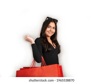 Woman with brown hair, black jeans and jersey holds a red shopping bag and smiles.