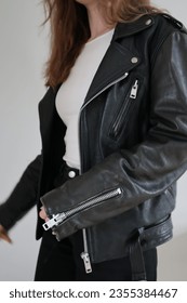 Woman with brown hair wearing a black vintage biker jacket. Black leather jacket. White background. White shirt. Minimalistic appearance. No faces. Curly hair. Calm atmosphere.