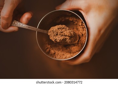 A woman with a brown manicure on her nails holds a jar of fragrant crumbly cocoa powder in her hands and scoops a portion with a silver teaspoon. A delicious drink in the morning. The cooking process. - Shutterstock ID 2080314772