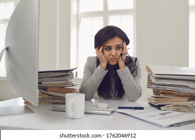 Woman brunette accountant in glasses with a mountain of documents on the table tired depressed emaciated disappointed depressive at the table in the office