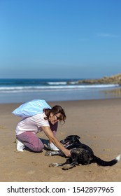 Woman brunette with dog picking up trash and plastics cleaning the beach. Environmental volunteer activist
