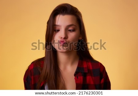 Woman with brunette hair showing fish face or duck face grimace with pout lips, fooling around, making ridiculous childish comical grimace. indoor studio shot isolated on pink background