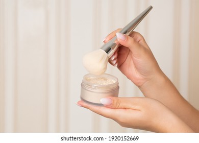 Woman with a brush using loose powder on a beige background. Empty space