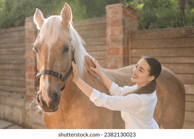 Woman brushing adorable horse outdoors. Pet care - Powered by Shutterstock