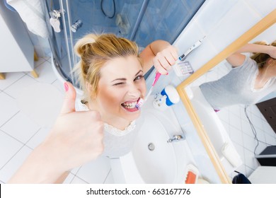 Woman brushing cleaning teeth closeup. Funny blonde girl with toothbrush in bathroom making thumb up hand sign gesture. Oral hygiene. Unusual wide angle top view