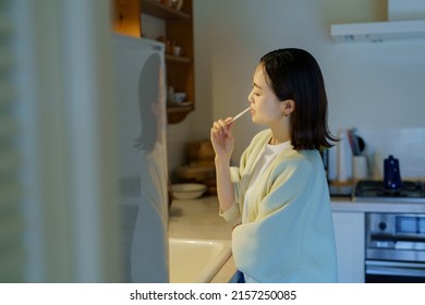 Woman Brushing Her Teeth In The Dark Kitchen At Night