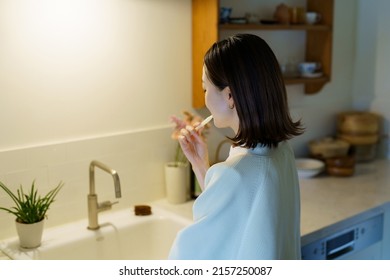 Woman Brushing Her Teeth In The Dark Kitchen At Night