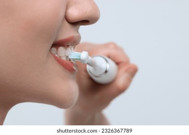Woman brushing her teeth with electric toothbrush on white background, closeup. Space for text