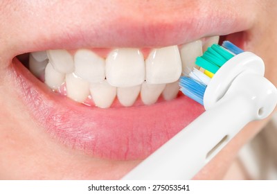 Woman brushing teeth with electric toothbrush, closeup