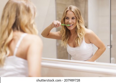 Woman Brushing Teeth In Front Of Mirror