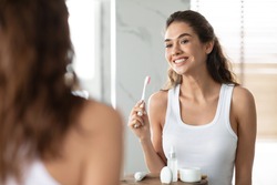 Woman Brushing Teeth Holding Toothbrush Smiling To Mirror In Bathroom