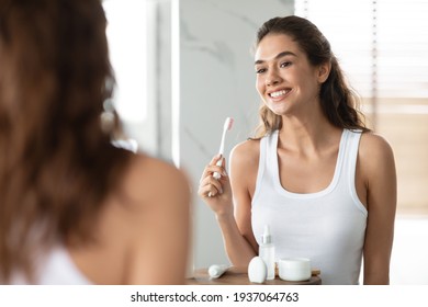 Woman Brushing Teeth Holding Toothbrush Smiling To Mirror In Bathroom