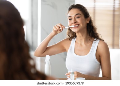 Woman Brushing Teeth With Toothbrush Standing Near Mirror In Bathroom