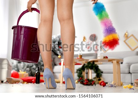 Woman with bucket and dusting brush in messy room after New Year party, closeup of legs