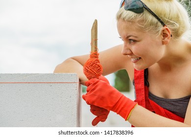 Woman builder using string as level in wall construction. Bricklayer, new house in progress.
