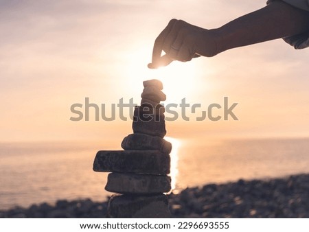 Woman building a cairn on the seashore at sunset. Zen relaxation and meditation concept