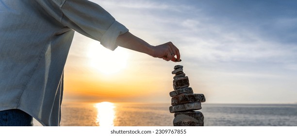 Woman building a cairn pyramide on the seashore at sunset. Zen relaxation and meditation - Powered by Shutterstock