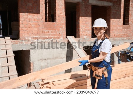 Woman building engineer in uniform and toolbelt holding timber girder