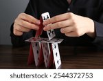 Woman building house of playing cards at wooden table, closeup