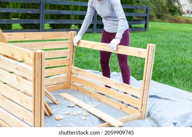 A Woman Is Building A Wooden Fence Or Keep On Tarp In Her Backyard. A Concept For Wood Work. Furniture Installation DIY Project. She Wears Gloves To Protect Against Wood Splinters