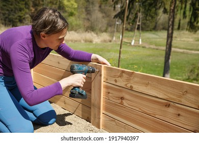 Woman Building A Wooden Frame For A Raised Garden Bed Using Power Drill. DIY Concept. Powerful Woman.