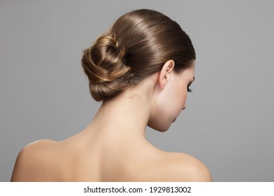 Woman with bun hairstyle on gray background. Bare back, shoulders and neck. Back view