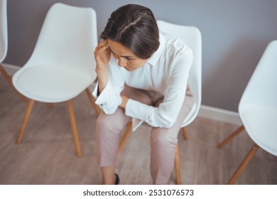 A woman in business attire appears stressed while sitting in a modern, minimalist waiting room. The scene captures feelings of anxiety and anticipation in a professional setting. - Powered by Shutterstock