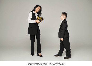 woman in business attire holding gift box near son with down syndrome in school uniform on grey - Powered by Shutterstock