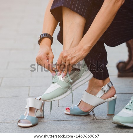 A woman in a business suit exchanges high-heeled shoes for sports shoes for a walk along a city street. Female legs pain and varicose veins concept.