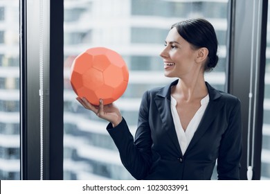 Woman In Business Suits And Black Varnished Shoes Play Football In The Office. They Play An Orange Soccer Ball