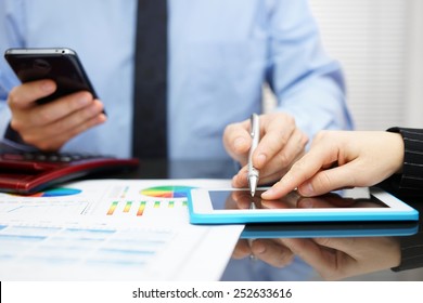 Woman And Businessman With Mobile Phone In Hand Reviewing Report On Tablet Computer