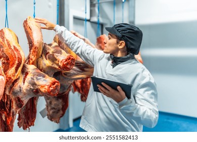 Woman butcher using digital tablet working inside a cold storage room in a meat processing factory - Powered by Shutterstock