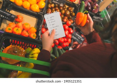 woman buy vegetables in supermarket with list of products. Bright fruit counter on background. paper and sweet pepper in hands.