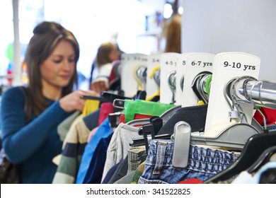 Woman Buying Children's Clothes In Charity Shop