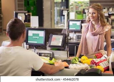 Woman Buying Food At Supermarket And Making Check Out With Cashdesk Worker In Store