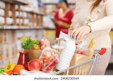 Woman buying fresh groceries at the supermarket, she is pushing a full shopping cart and holding a bottle of milk - Powered by Shutterstock