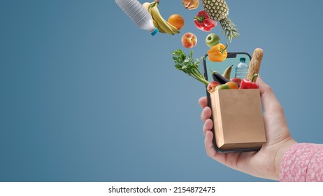 Woman buying groceries online using her smartphone: full grocery bag miniature on a smartphone screen - Shutterstock ID 2154872475