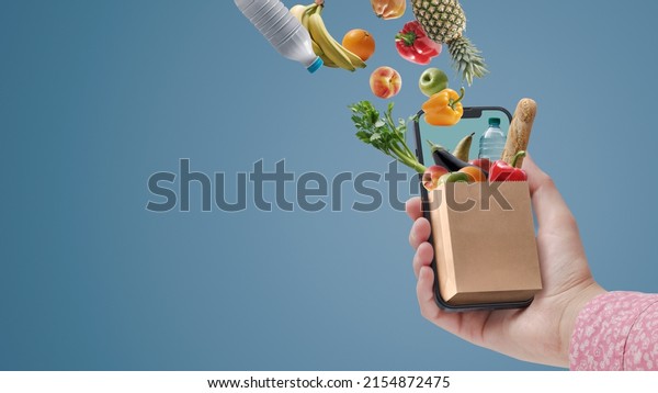 Woman buying groceries\
online using her smartphone: full grocery bag miniature on a\
smartphone screen