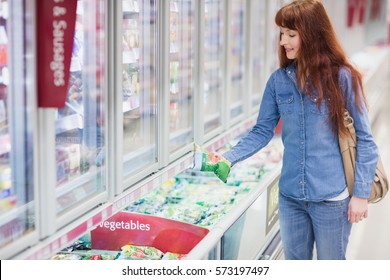 Woman Buying Vegetables In Frozen Section In Supermarket