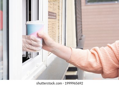 Woman Buys Takeaway Hot Drink. A Gloved Hand Brings A Disposable Glass Out Of The Window. Street Food Kiosk.