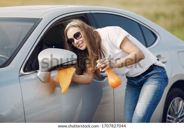 Woman by the car. Lady in a white t-shirt. Woman\
wipes the car
