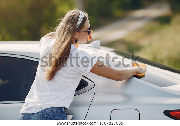 Woman by the car. Lady in a white t-shirt. Woman
wipes the car