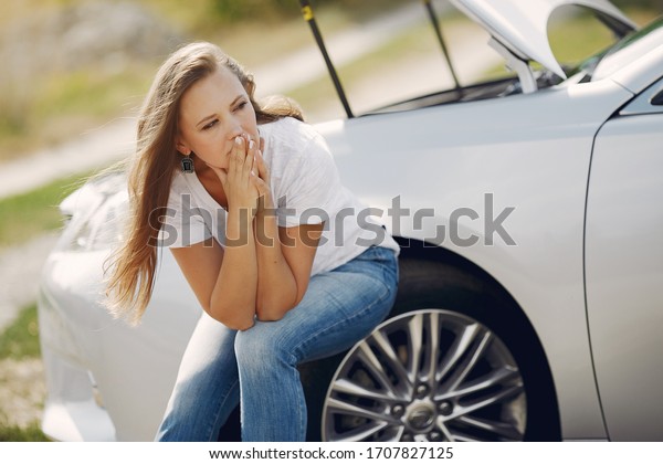 Woman by the car. Lady in a white t-shirt. Broken\
car. Woman need to help.