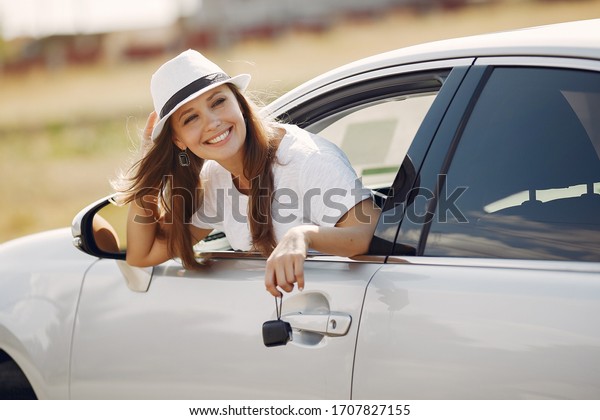 Woman by the car. Lady in a white t-shirt. Famale in\
a white hat.