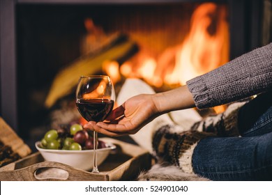 Woman By The Fireplace. Woman In Woolen Socks Taking A Glass Of Red Wine Relaxing By The Cozy Fireplace. Snug Winter Evening.