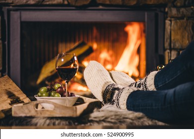 Woman By The Fireplace. Woman In Woollen Socks Taking A Glass Of Red Wine Relaxing By The Cozy Fireplace. Snug Winter Evening.