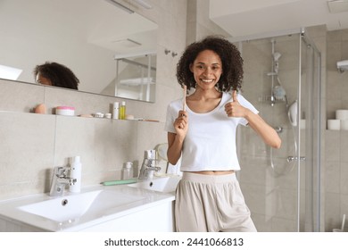 A woman by the sink in a bathroom, brushing her teeth and giving a thumbs up - Powered by Shutterstock