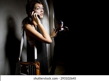 Woman Calling 911 With A Cell Phone While Alone In A Dark Street Alley.  A Criminal Is Stalking Her From The Shadows.  She Is Calling For Help.